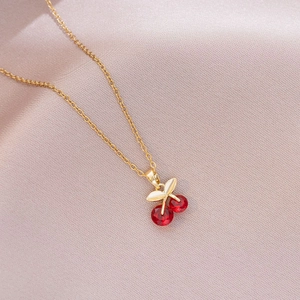 Macro shot of cherry pendant necklace with red crystals and gold finish on silk fabric