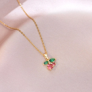 Minimalist cherry pendant necklace with pink and green gems on a soft pink satin fabric