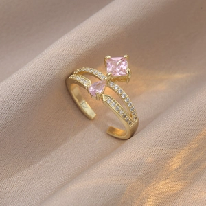 Détail d'une bague dorée avec zircons roses carrés et goutte sur satin champagne