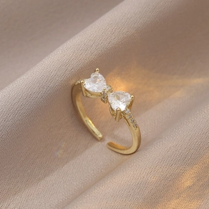 Gros plan d'une bague nœud dorée avec zircons en cœur et petits cristaux pavés