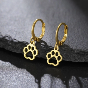 Detailed close-up of gold stainless steel hollow paw print earrings on black stone