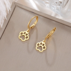 Detailed close-up of gold hollow pet paw earrings on a decorative feather background