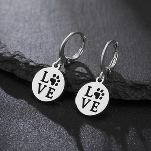 Detailed macro of silver stainless steel love earrings with paw print on black rock