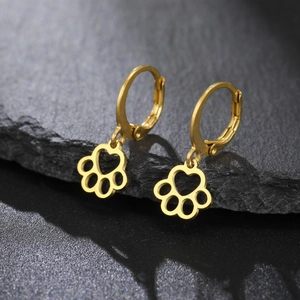 Close-up of golden hollowed paw print earrings with heart cutout on dark textured stone
