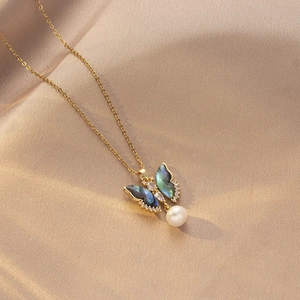Detalle del collar de mariposa con alas iridiscentes y un colgante de perla redonda