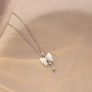 Detalle del colgante de mariposa con nácar blanco y circonitas sobre seda dorada