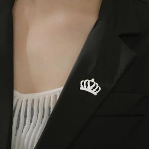 Détail macro d'une broche couronne argentée avec découpe cœur sur un revers de blazer noir