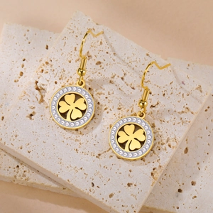 Détail de boucles d'oreilles trèfle doré avec zircons sur un support en pierre texturé