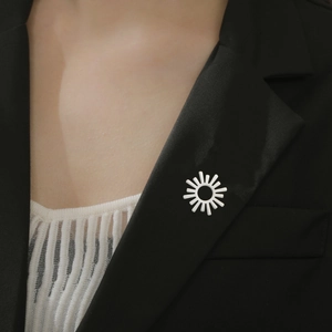 Détail d'une broche rayon de soleil blanche épinglée sur le revers d'un blazer noir