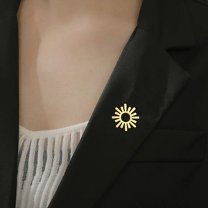 Broche soleil doré avec anneau évidé épinglée sur le revers d'un tailleur noir