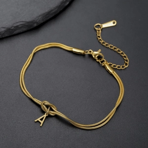 Detail van de gouden dubbele slangschakelarmband met een knoop en letter A hanger