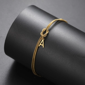Detailopname van een gouden slangenketting armband met knoop en hanger met de letter A