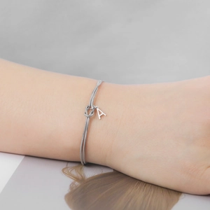 Detail van zilveren knoopslangenarmband met hangende hoofdletter A bedeltje om de pols