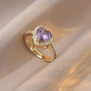 Détail d'une bague cœur en zircon violet avec monture pavée dorée sur tissu satiné