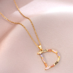Détail d'un collier en titane doré avec pendentif lettre D serti de zircons multicolores