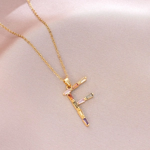 Vue détaillée du pendentif lettre F dorée avec zircons colorés sur fond satiné rose