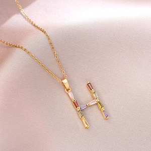 Vue détaillée du pendentif H doré serti de zircons colorés sur du satin rose chic