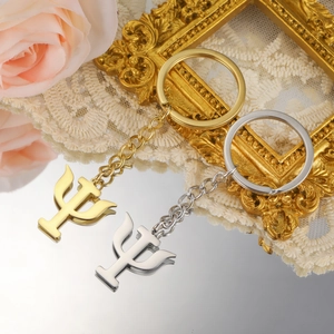 Polished gold and silver Psi Greek letter keychains on a reflective surface