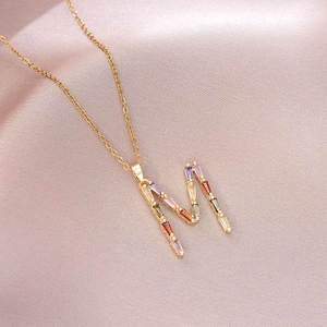 Gros plan du collier lettre M doré orné de pierres multicolores sur satin rose