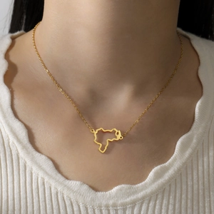 Close-up of a hollow out gold stainless steel map pendant necklace worn by a model
