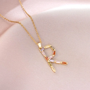 Détail du collier en titane doré avec pendentif lettre R orné de cristaux multicolores