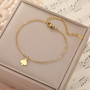 Detail of gold heart pendant and lobster clasp on stainless steel cross chain bracelet