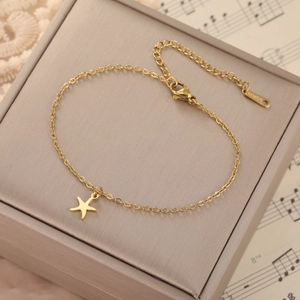 Macro detail of gold starfish pendant on a thin cross chain with S-STEEL engraved tag