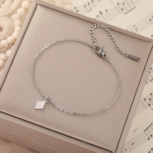 Detailed view of stainless steel chain bracelet with heart pendant on beige jewelry box