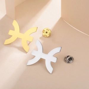 Close-up of gold and silver Pisces zodiac pins with metallic finish on geometric background