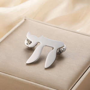 Detailed close-up of polished 304 stainless steel Chai symbol brooch on silk packaging