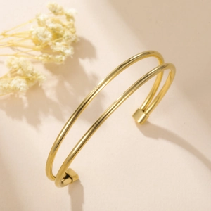 Detalle macro del brazalete abierto de doble capa dorado sobre un fondo de tonos cálidos