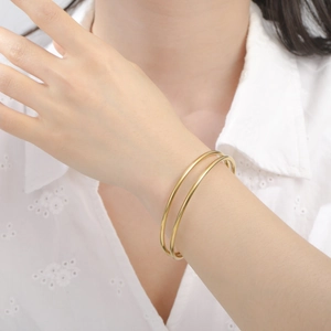 Primer plano de un brazalete dorado de doble capa en una muñeca con encaje blanco