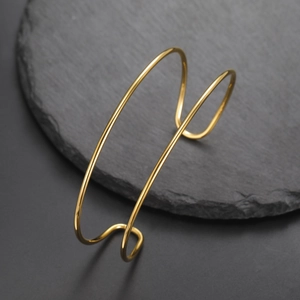 Primer plano de brazalete dorado minimalista de doble línea sobre base de piedra