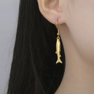 Detailed close-up of a gold fish-shaped earring being worn with textured scale details