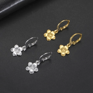 Dettaglio di orecchini a fiore a cinque petali in oro e argento su sfondo nero opaco