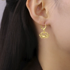 Close-up of a golden crab charm huggie hoop earring worn by a model for a beach style