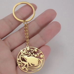 Detailed view of a golden stainless steel fox and cherry blossom pendant keychain on a hand