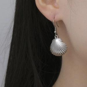 Close-up of a silver scallop shell drop earring showing metal texture and fit on ear