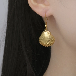 Macro shot of gold stainless steel shell pendant earring worn on a model's ear