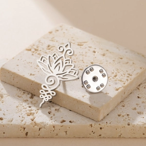 Detailed view of silver stainless steel lotus brooch on decorative beige stone props