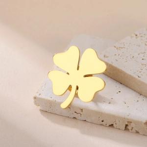 Polished gold four-leaf clover brooch displayed on minimalist beige travertine stones