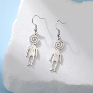 Close-up of minimalist stainless steel alien humanoid earrings on a textured stone display