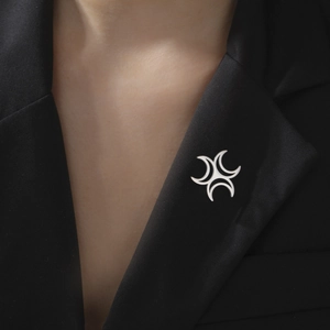 Close-up of a silver crescent geometric brooch pinned on a black suit lapel