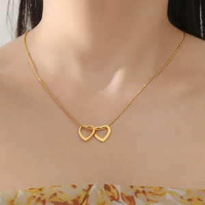 Détail du collier doré à deux cœurs entrelacés avec des perles sur une chaîne fine