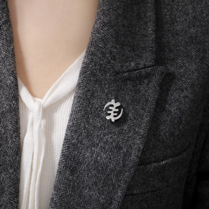 Polished silver stainless steel Gye Nyame cross brooch pinned on a grey wool blazer