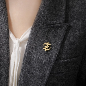 Detail of golden Gye Nyame cross brooch pinned on a grey herringbone suit lapel