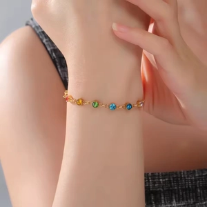 Primer plano de una pulsera de cadena dorada con siete cristales de colores en la muñeca