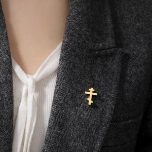 Detail of a golden Orthodox cross brooch on a classic herringbone blazer with white shirt