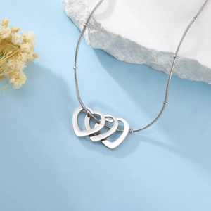 Détail du pendentif triple cœur argenté sur une chaîne serpent sur texture pierre blanche