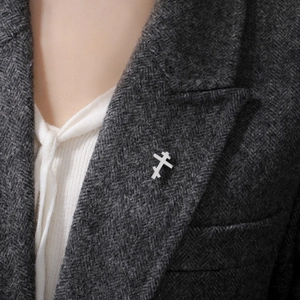 Minimalist silver stainless steel orthodox cross brooch pinned to a grey wool coat lapel